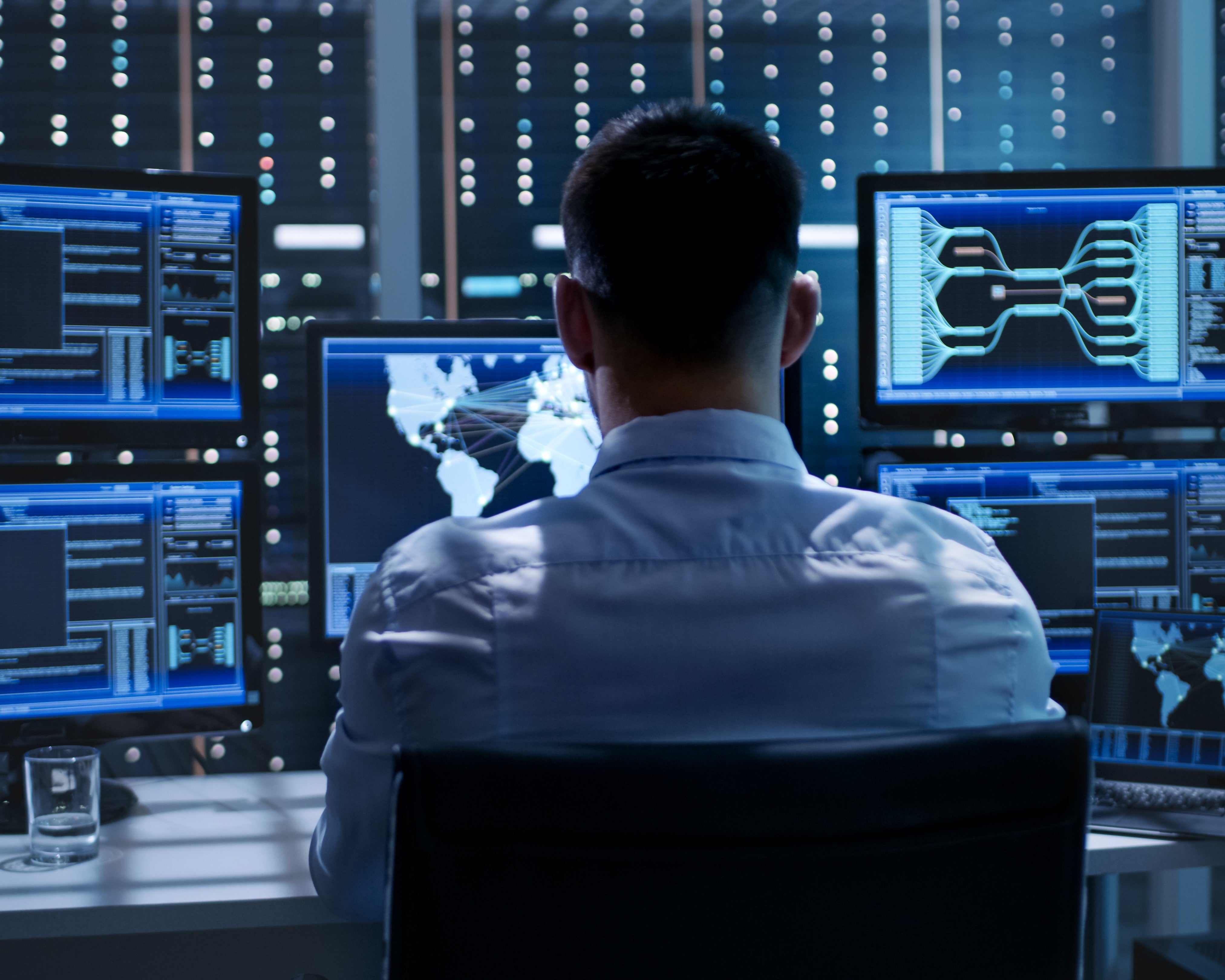 A man sitting at a desk with multiple monitors, working on a laptop.